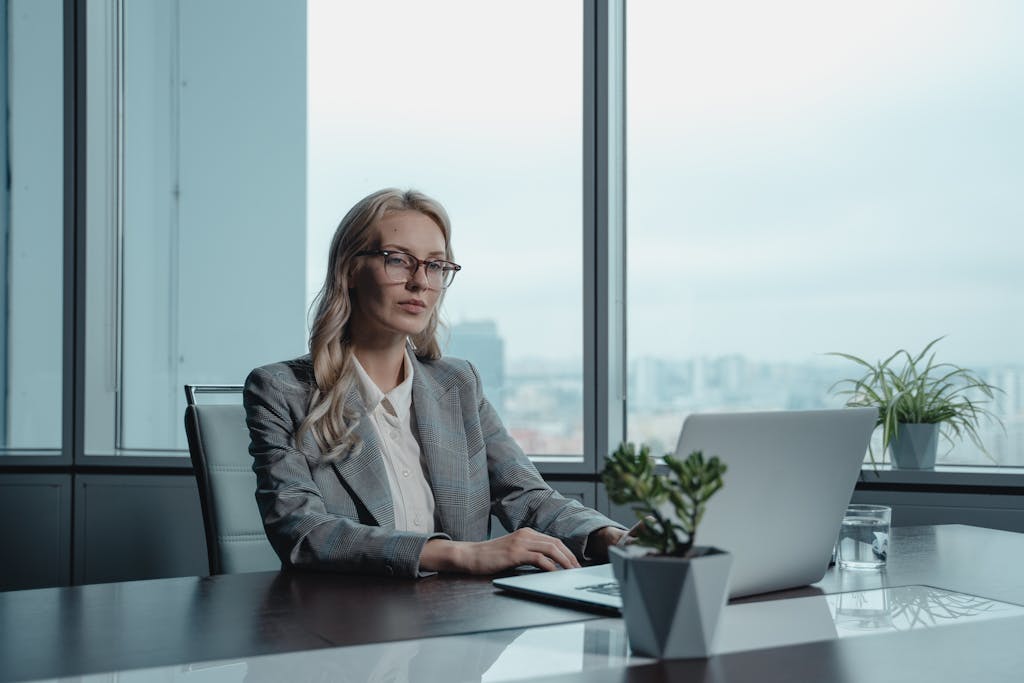 Introvert leadership - A confident businesswoman in a grey suit working on a laptop in a modern office setting.
