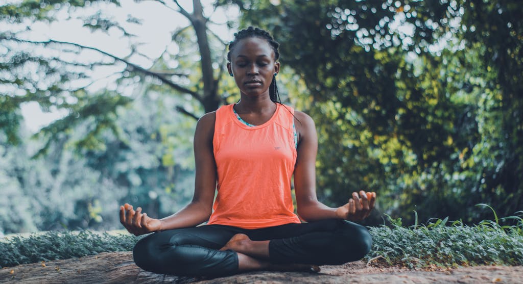 Introvert health. A woman meditating peacefully outdoors in a lush green setting, promoting relaxation and mindfulness.