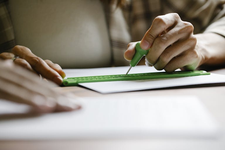 Close-up of hands using a stylus and ruler to write Braille on paper. Inclusive education concept.