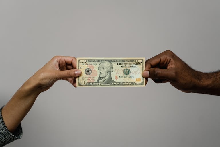 Close-up of two hands exchanging a ten dollar bill, symbolizing financial transaction or exchange.