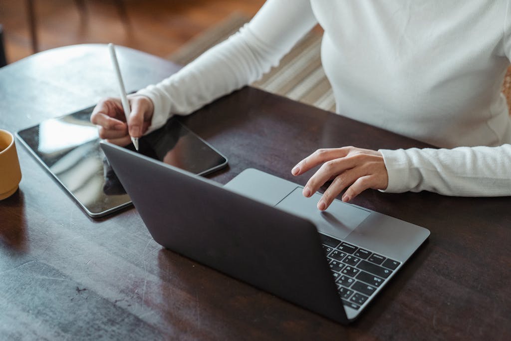Focused businesswoman multitasking with a laptop and tablet in a modern office setting.