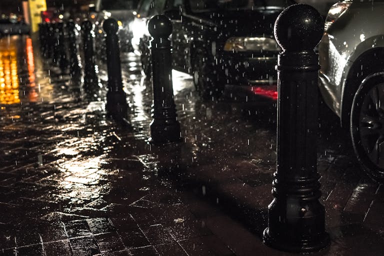 Urban street scene at night with rain and glistening pavement reflecting city lights.