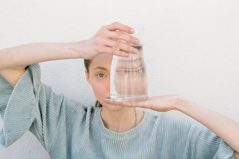 Woman holding a glass jug reflecting her face, creating a unique visual distortion.