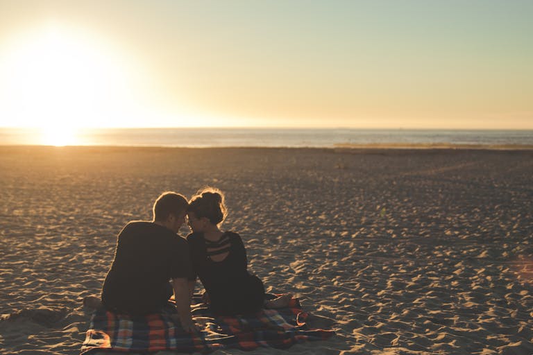 A couple enjoys sunset together on a sandy beach, capturing a moment of love and togetherness.