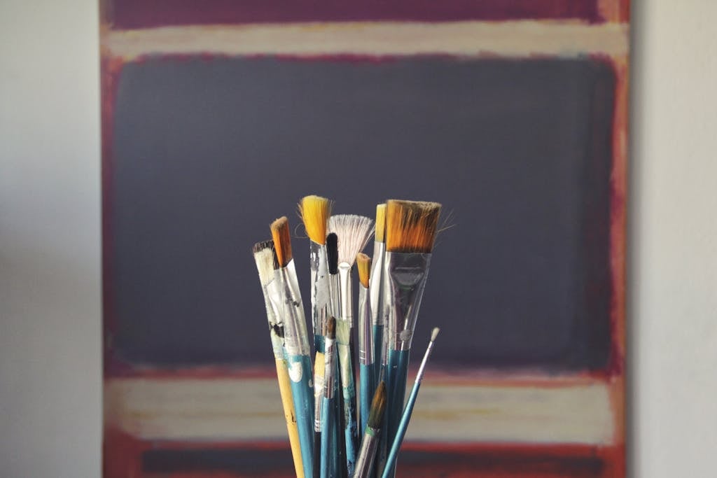A set of paintbrushes in front of an abstract canvas, reflecting creativity and inspiration.