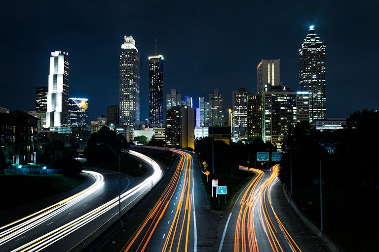 A vibrant cityscape at night showcasing light trails on the highway beneath towering skyscrapers.