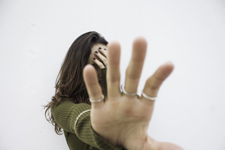 A woman covering her face with an extended hand against a white background.