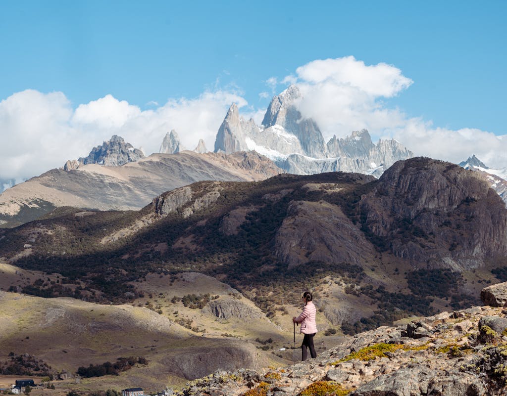 A woman hikes in the stunning mountainous terrain with a clear blue sky overhead.