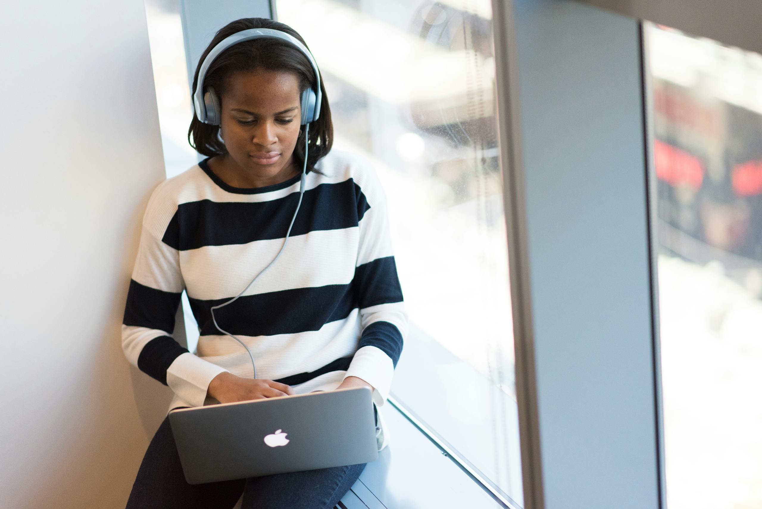 Professional woman with headphones working on laptop by sunny window in calm home environment
