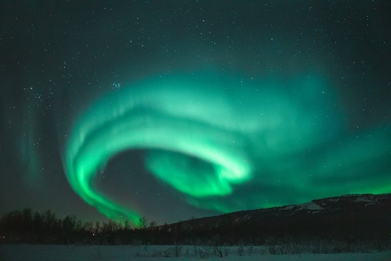 Captivating view of the Northern Lights dancing above a snowy landscape under a starry night sky.