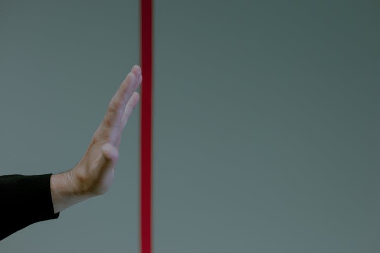 Close-up of a man's hand gesturing stop in front of a vertical red line, concept of boundary.