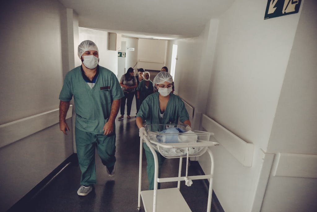 Healthcare workers in surgical attire transporting a newborn in a hospital corridor.