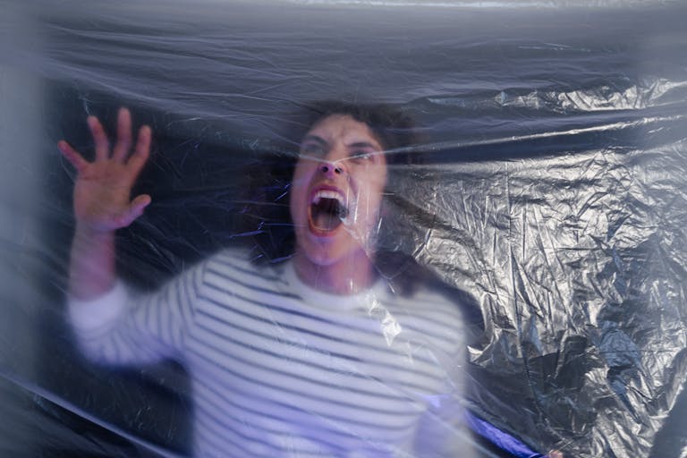 Man in striped shirt screaming behind translucent plastic foil, conveying fear.