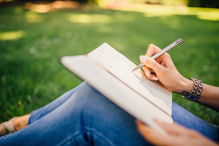 Person sitting peacefully in nature thinking and writing in a notebook