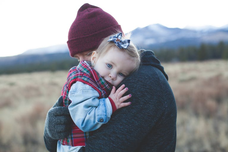 A father and child embrace outdoors with a winter mountain backdrop.