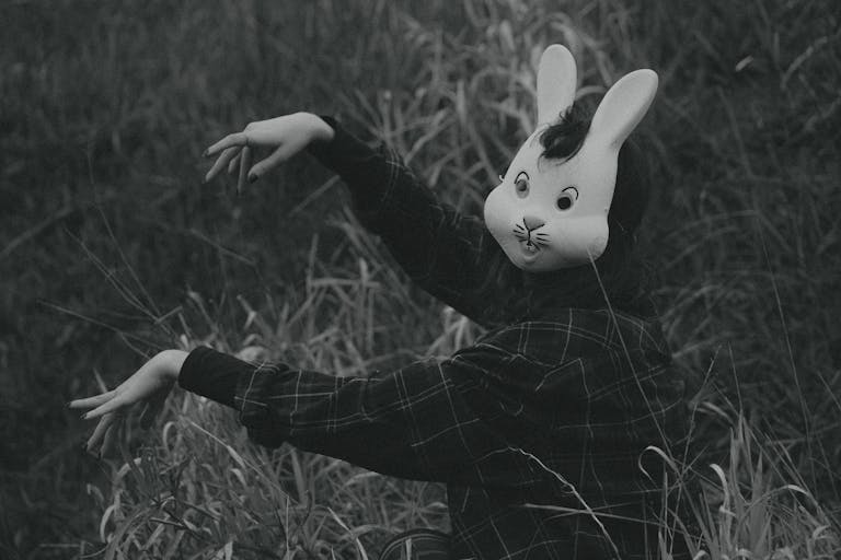 A mysterious figure wearing a rabbit mask poses in tall grass, creating an eerie atmosphere.