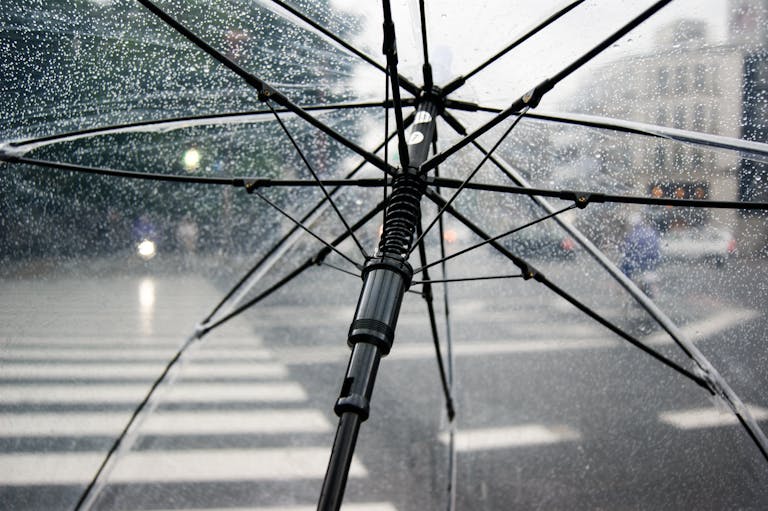 Close-up of a transparent umbrella with raindrops in an urban street setting.