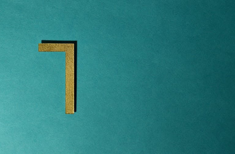 Minimalist image of a golden numeral seven on a teal background, ideal for decorative use.
