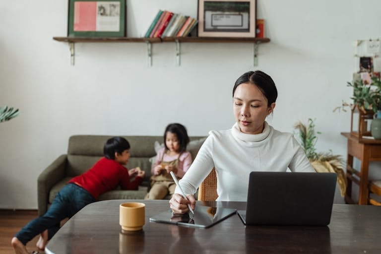 Mother on laptop while child plays nearby, illustrating how introvert parents can integrate friendship into family life