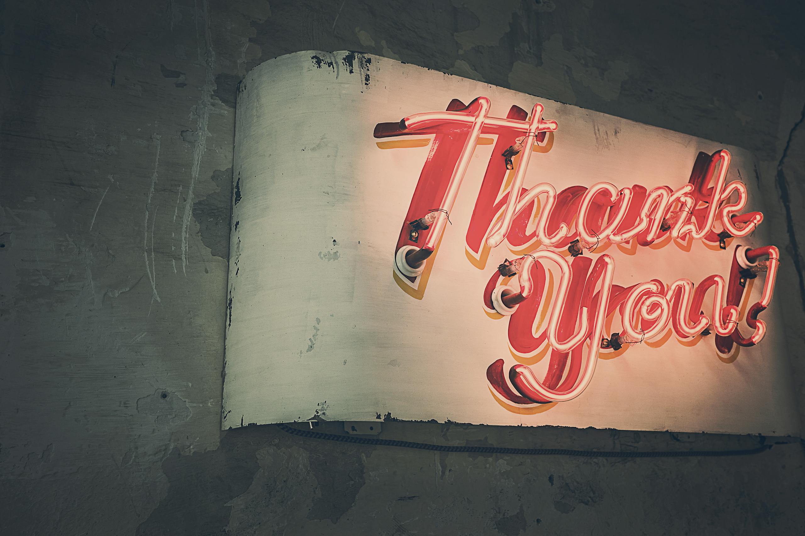 Retro neon 'Thank You' sign glowing warmly against a rustic wall, creating a nostalgic ambiance.