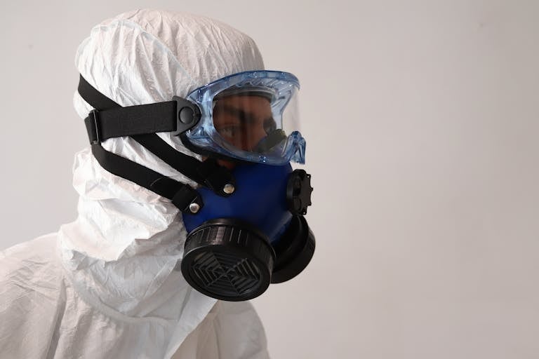 Side view of a person in protective suit wearing a gas mask against a white background.