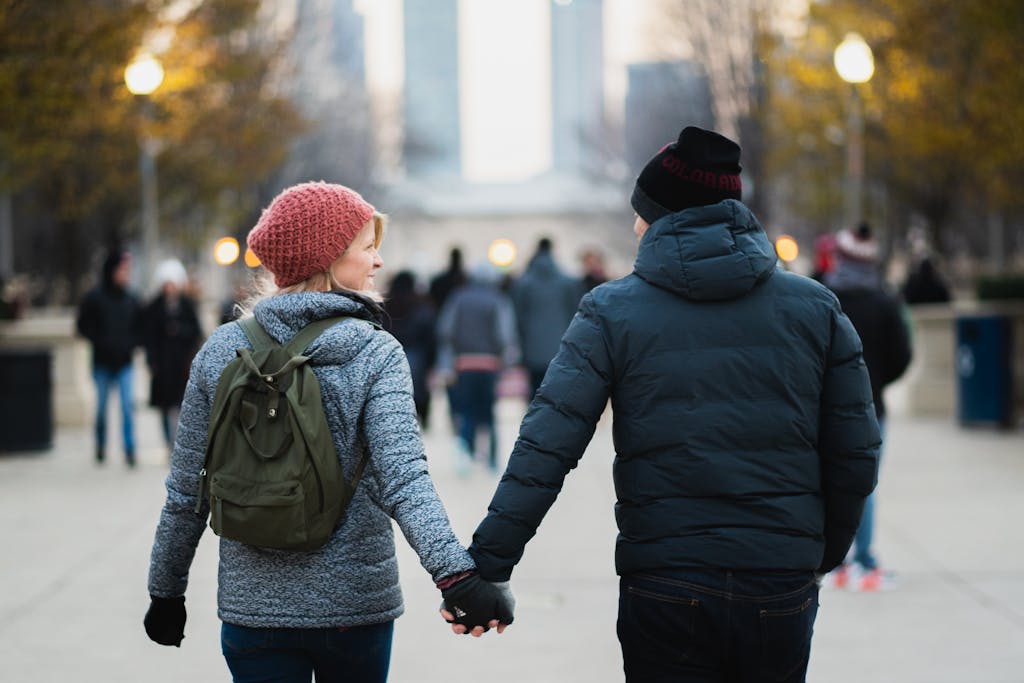 A couple holds hands on a winter day in an urban park, capturing warmth and connection.