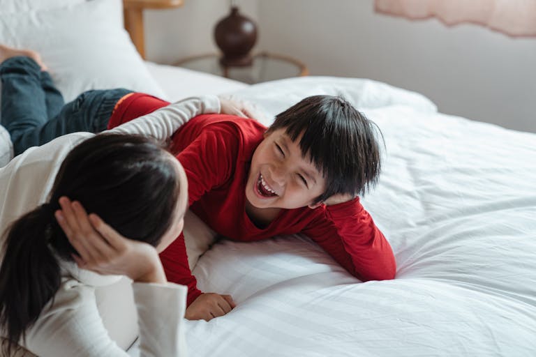 A mother and son lying on a bed sharing a joyful moment filled with laughter and love.