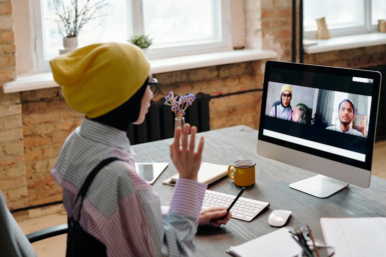 Designer participating in a video call from home office with organized notes and design work visible on screen