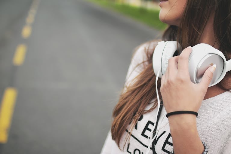 Close-up of a woman outdoors holding headphones, enjoying music on a quiet road.