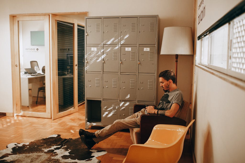 A relaxed man sits in a contemporary office, featuring lockers and stylish furniture, creating a cozy workspace.