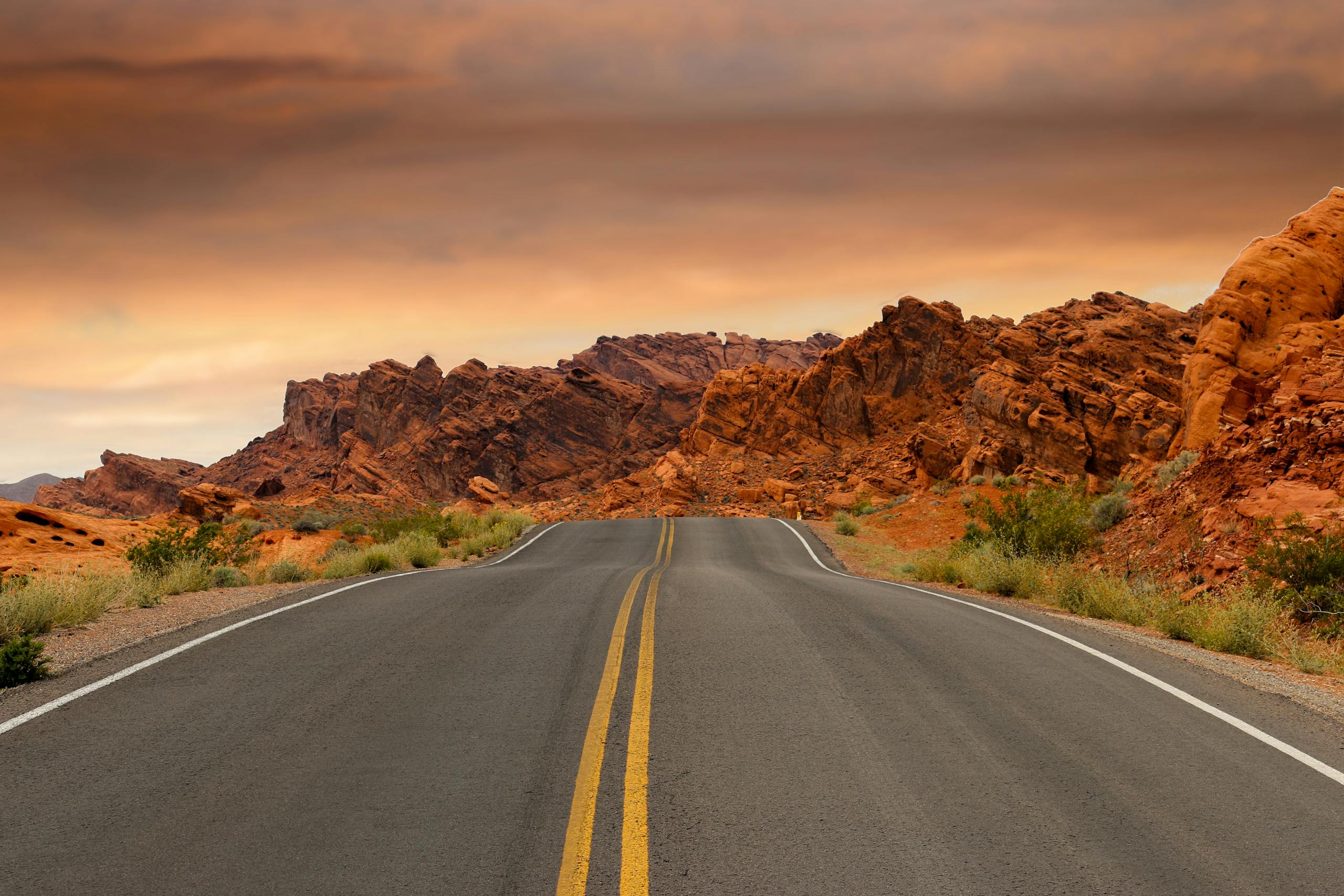 A scenic highway winds through dramatic red desert rock formations under a colorful sunset sky.