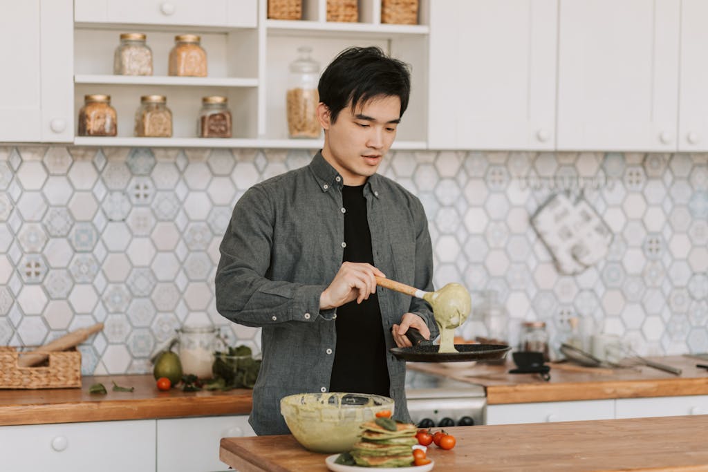 A young man cooking pancakes in a stylish kitchen setting with a focus on culinary skills.