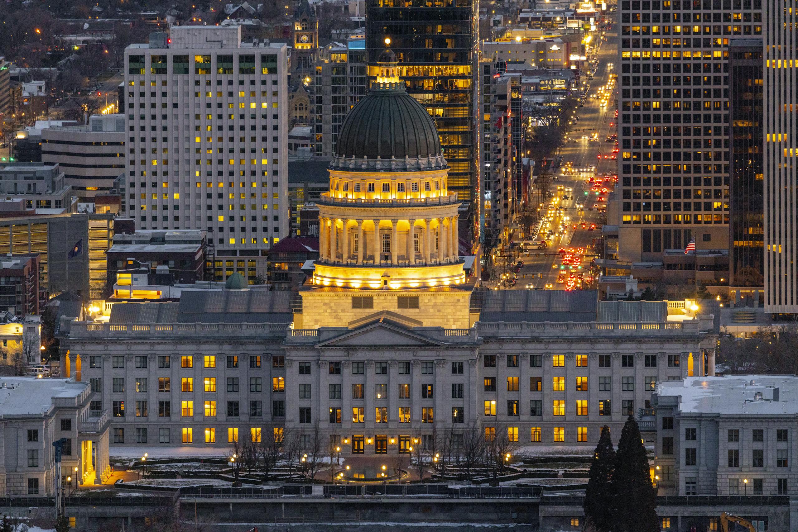 Aerial view of the illuminated Utah State Capitol at night in Salt Lake City amidst downtown buildings.