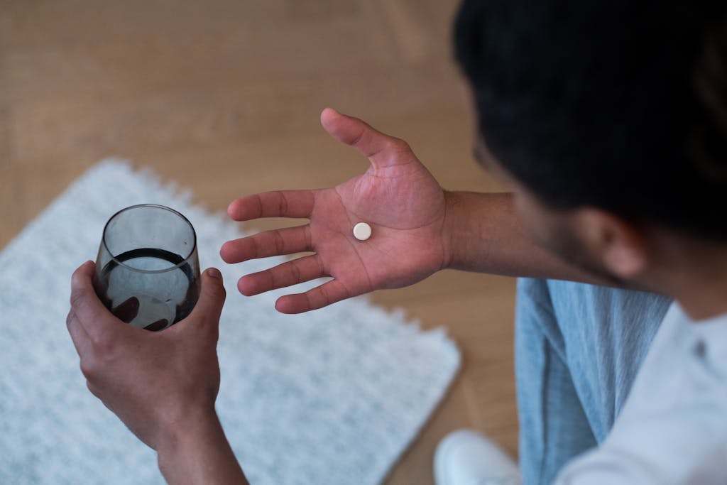 Close-up of a man about to take medication with water, indoors.