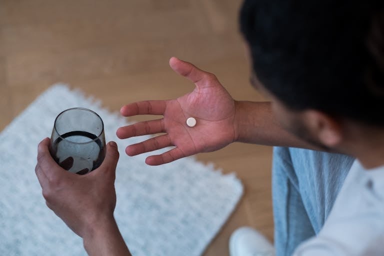 Close-up of a man about to take medication with water, indoors.