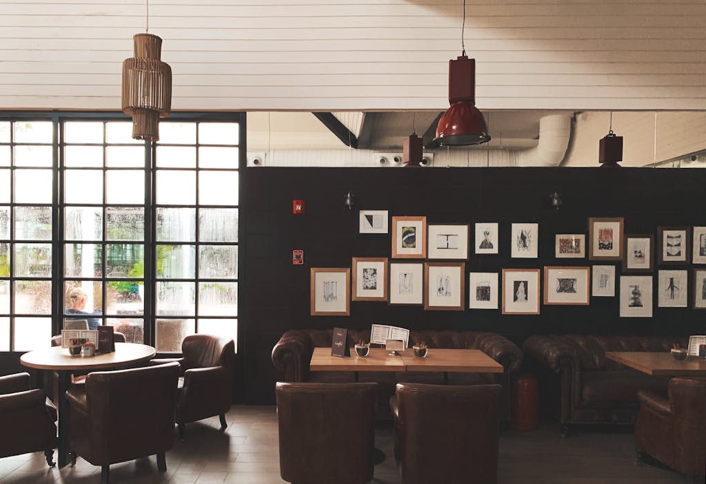 Cozy café interior featuring leather chairs, framed wall art, and pendant lighting. Ideal for meetings.