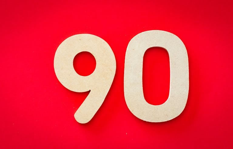 Minimalist depiction of wooden numbers '90' against a vivid red backdrop, capturing simplicity and elegance.