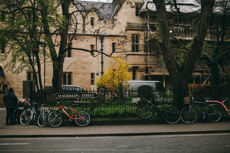 Parked bicycles on Magdalen Street, Oxford, with a historic building backdrop, showcasing urban outdoor life.