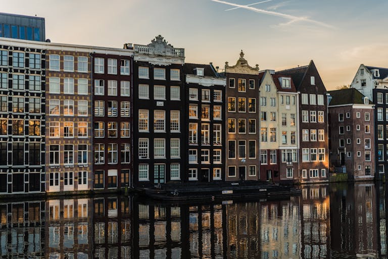 Scenic view of iconic canal houses in Amsterdam with reflections in the water during sunset.