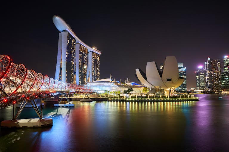 Stunning night view of Marina Bay Sands and Helix Bridge illuminated over water in Singapore.