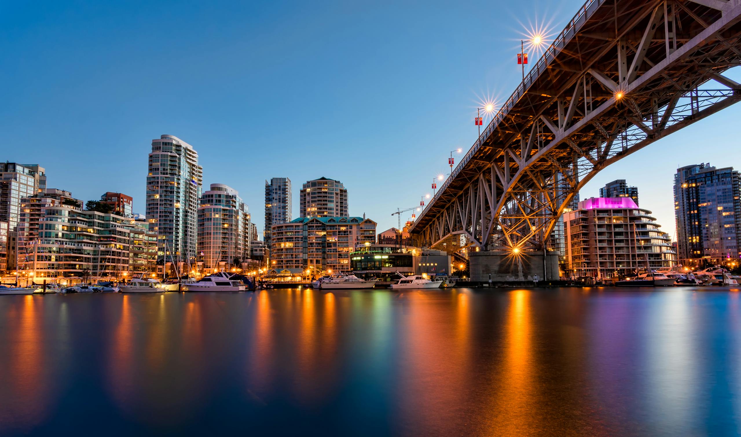 Stunning Vancouver cityscape view from Granville Bridge at dusk with illuminated buildings and reflections.