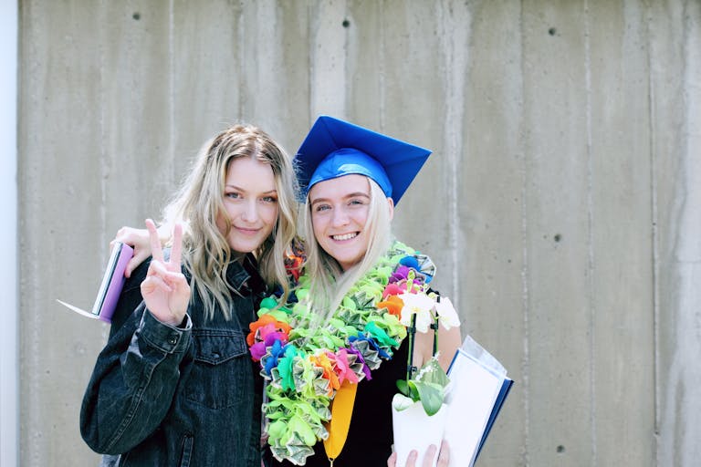 Two young women celebrating graduation outdoors with joy and vibrant colors.