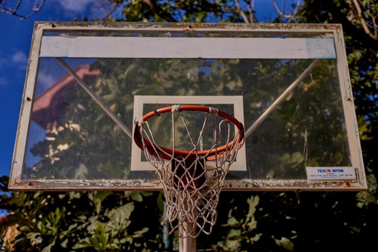 Weathered outdoor basketball hoop with red rim against blue sky and trees