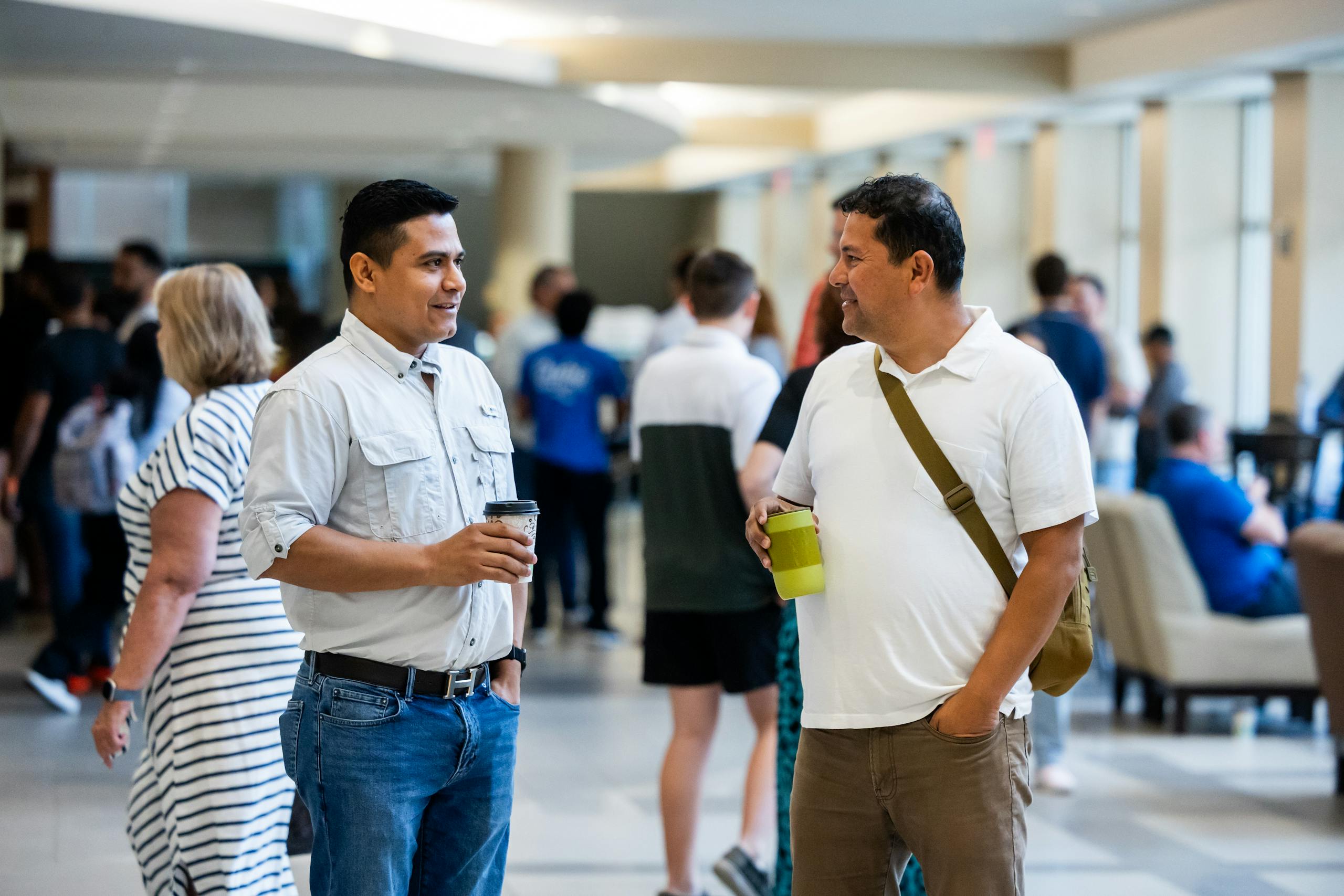 Two men engage in friendly conversation at a community event, holding beverages.