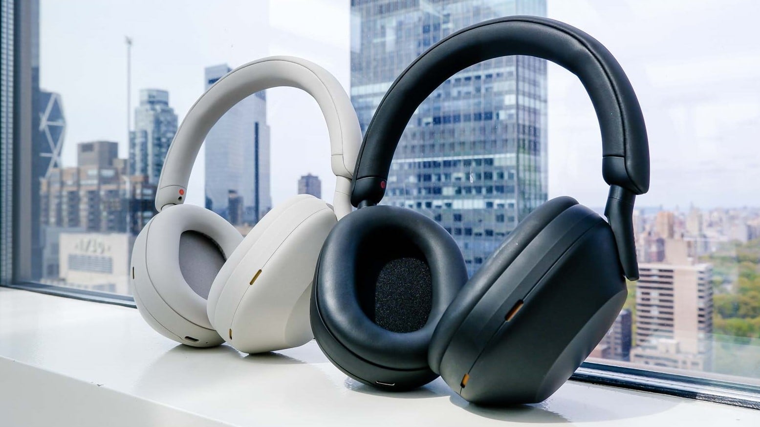Two premium headphones in white and black against urban skyline window view