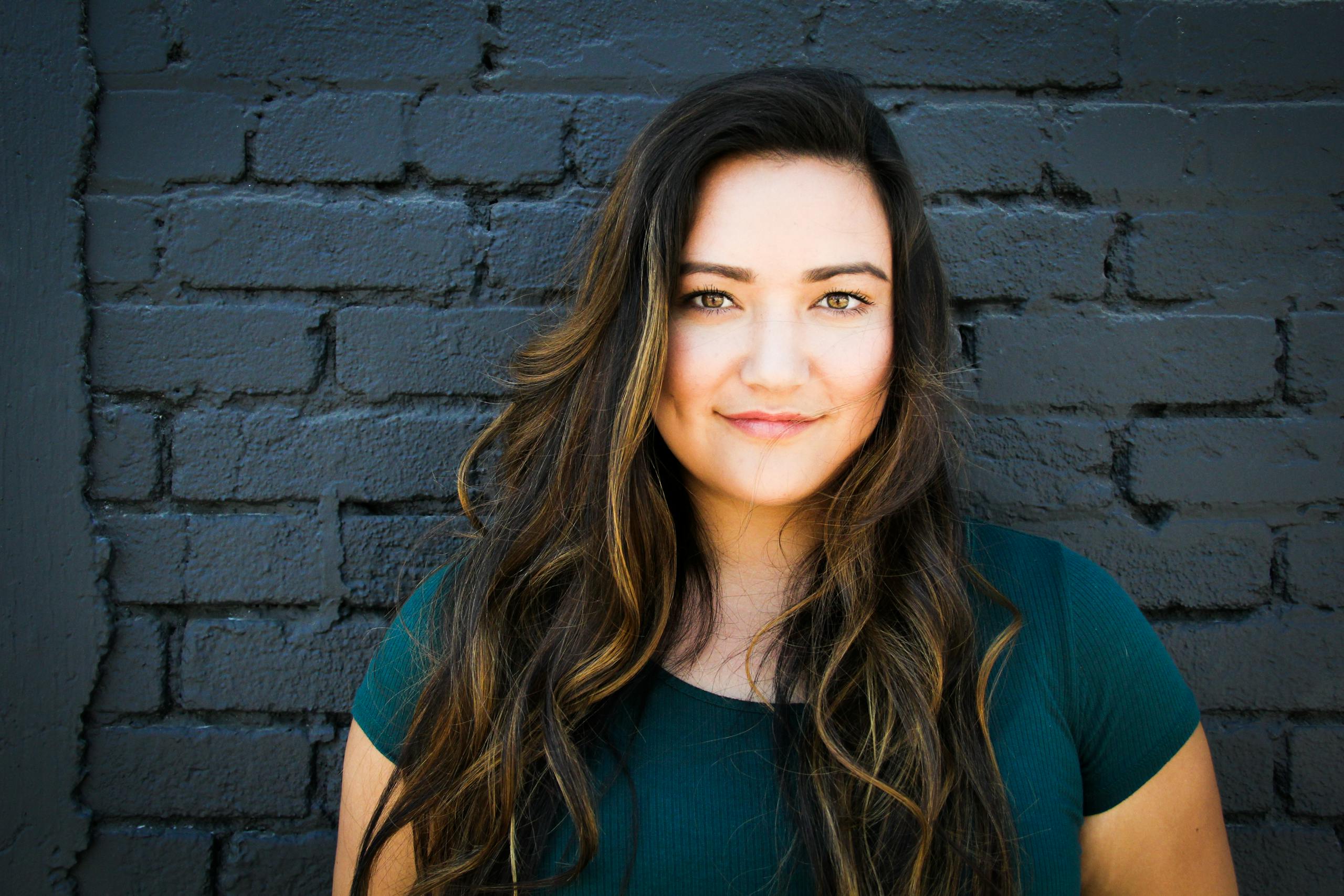 Portrait of confident woman with long brunette hair smiling in front of brick wall.