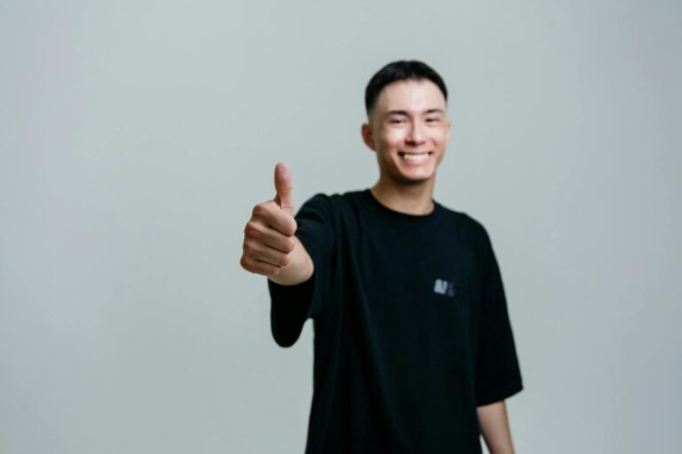 Cheerful young man in black shirt smiles and gives thumbs up studio setting