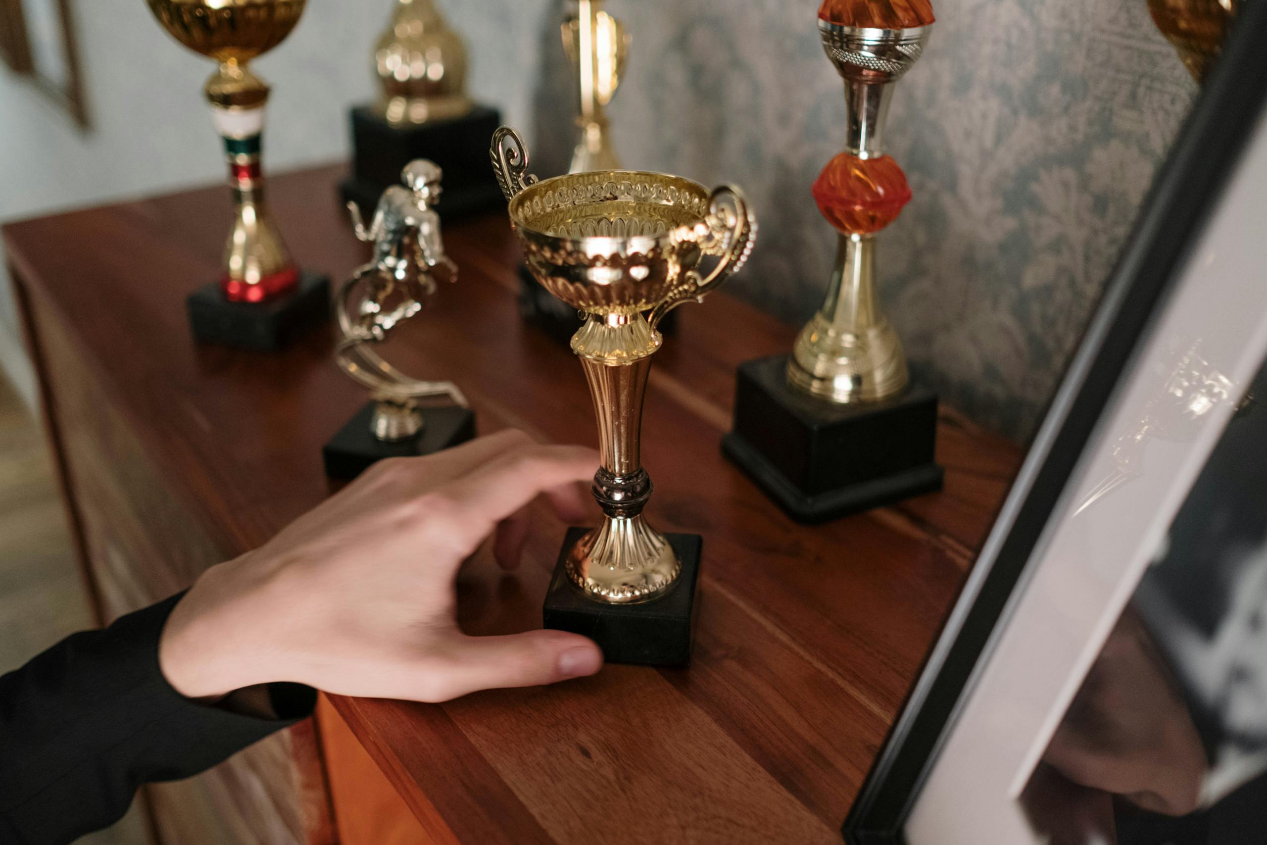 Close-up of hand reaching for shiny trophy on wooden shelf symbolizing success