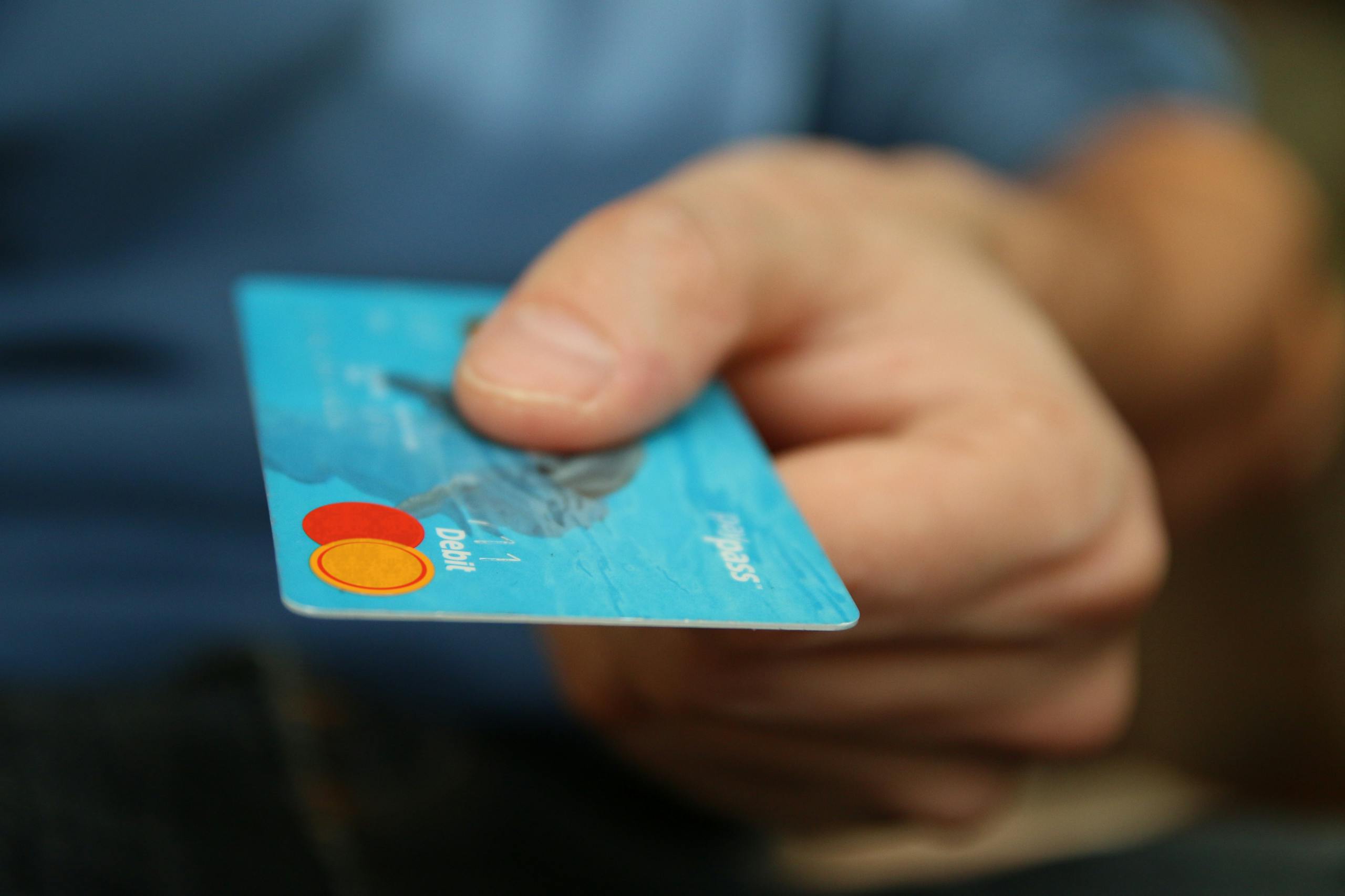 Close-up of hand offering blue debit card for payment transaction.