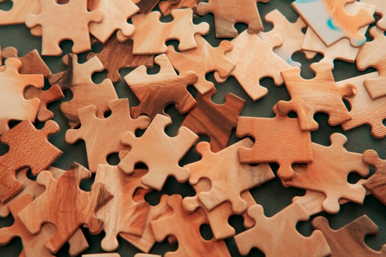 Close-up view of scattered wooden jigsaw puzzle pieces on dark surface.